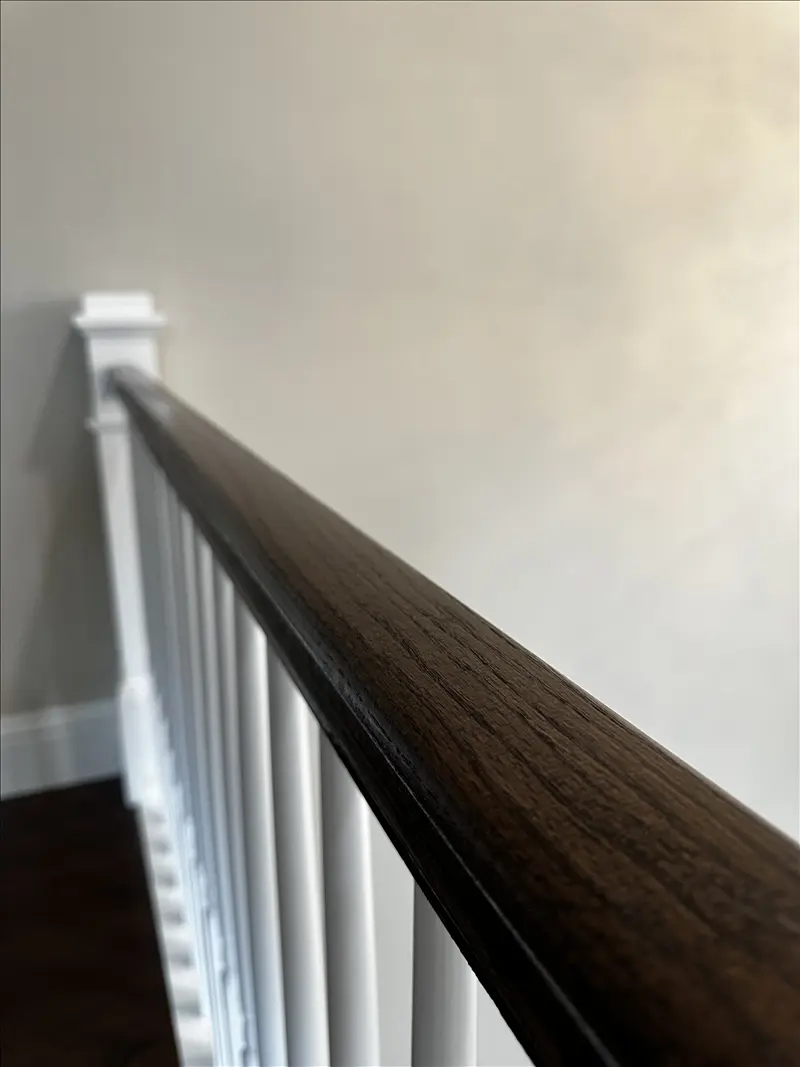 Dark stained stair handrail with crisp white balusters and smooth painted wall